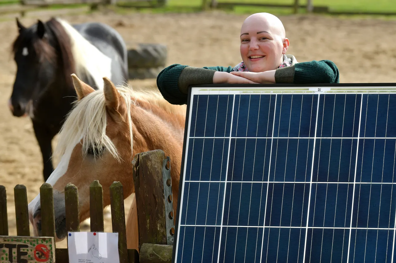 Frau steht hinter Solarmodul, daneben stehen zwei Pferde