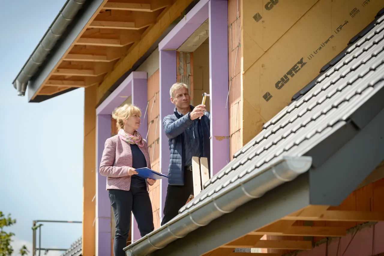 Energieberaterin und Dämmexperte stehen auf Dachstuhl und Messen die Dämmung an großen Dachfenstern.