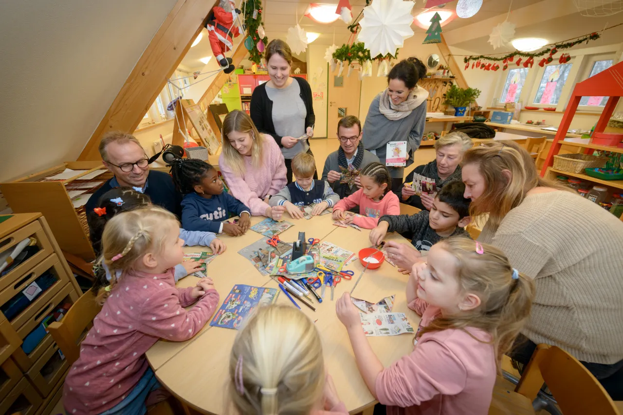 Kinder basten am Tisch, Projektpartner von enerkita stehen um Tisch herum