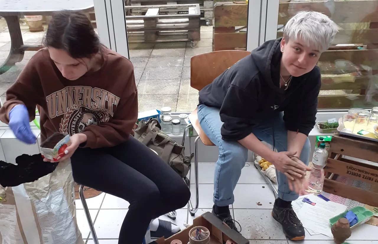 Zwei Teenager sitzen auf Stühlen uns füllen kleine Behälter mit Erde