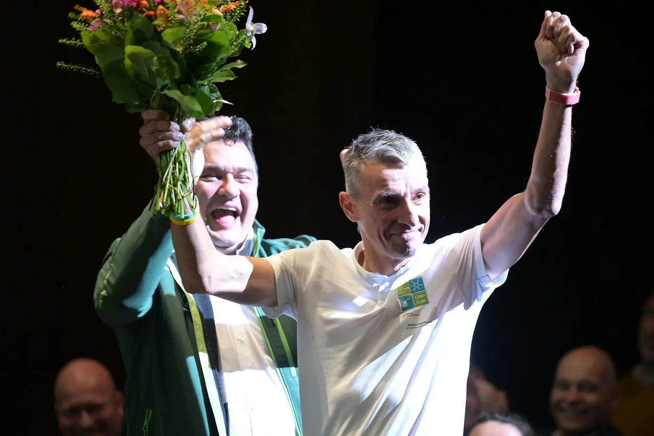 Sieger hält die Arme feiernd nach oben - in der einen Hand hält er einen Blumenstrauß