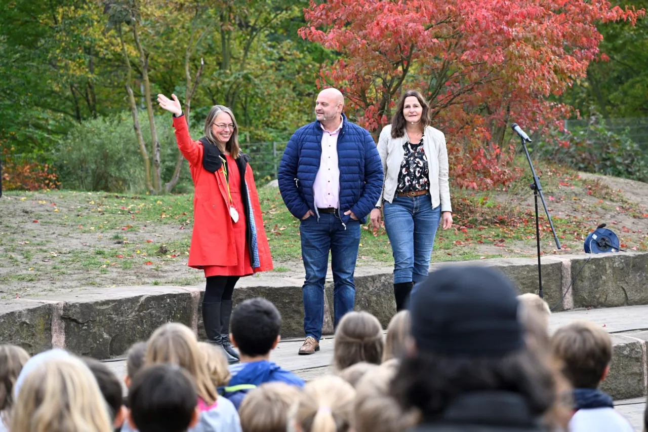 Senatorin Sascha Aulepp steht auf Bühne und winkt, neben ihr Schulleiter Kirst und eine Schuleiterin Barthe