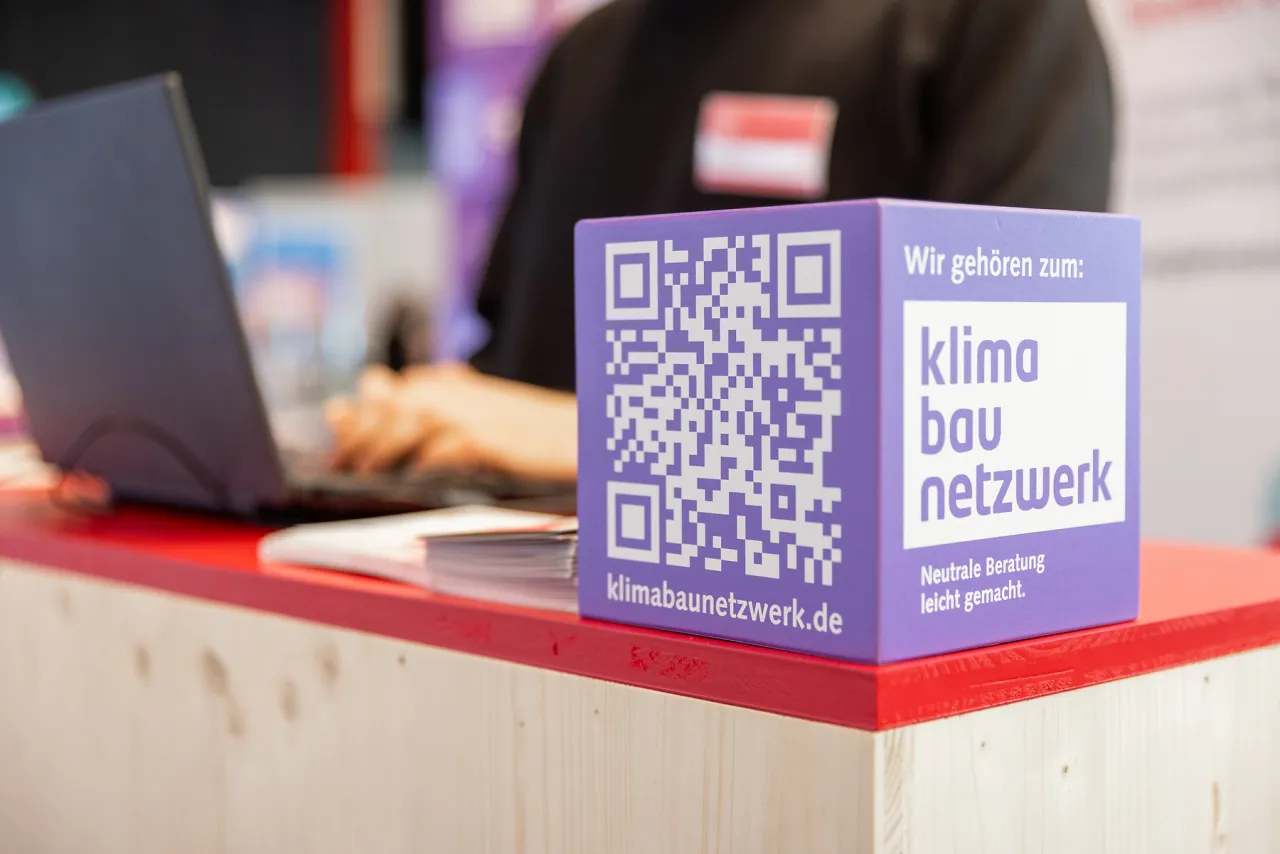 Im Bild: Holzw&uuml;rfel auf einem Tresen an einem Messestand. Der W&uuml;rfel zeigt die Zugeh&ouml;rigkeit zum Klima Bau Netzwerk - einem Zusammenschluss etablierter Beratungsinstitutionen mit langj&auml;hriger Erfahrung in den Bereichen Bauen, Wohnen und Modernisieren in Bremen und Bremerhaven.