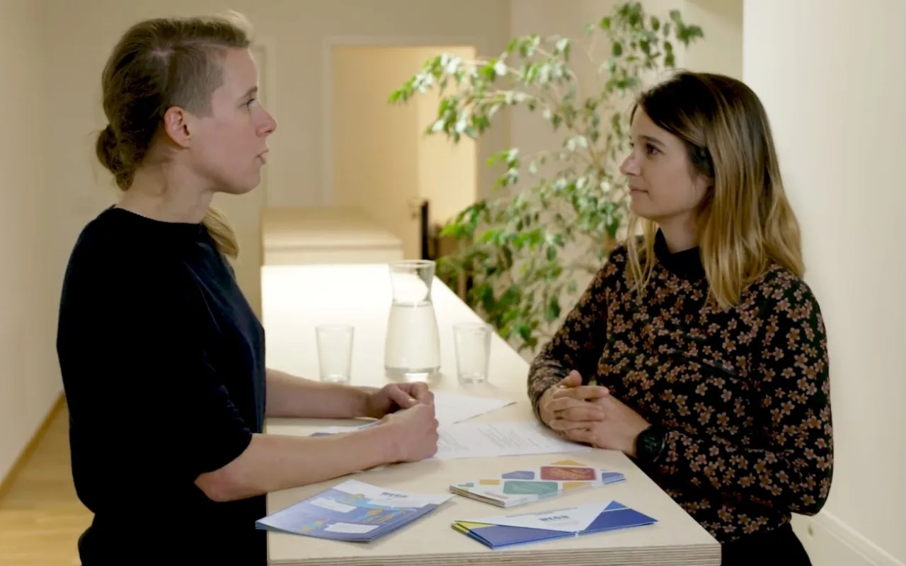 Zwei Frauen sprechen an einem Tresen, Beratungssituation