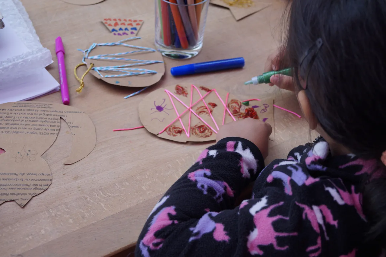Blick über die Schulter, Mädchen bastelt einen Fisch und hält Stift in der Hand