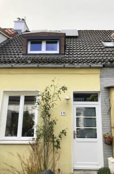 Außenansicht eine einstöckigen Reihenhauses mit gedämmter, gelb gestrichener Fassade