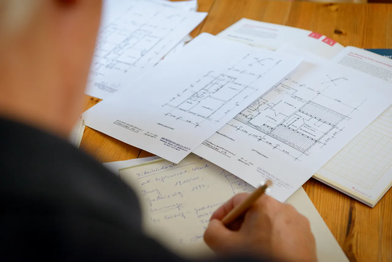 Blick über Schulter auf Hausumrisse und einen Notizblock, auf dem eine Person schreibt