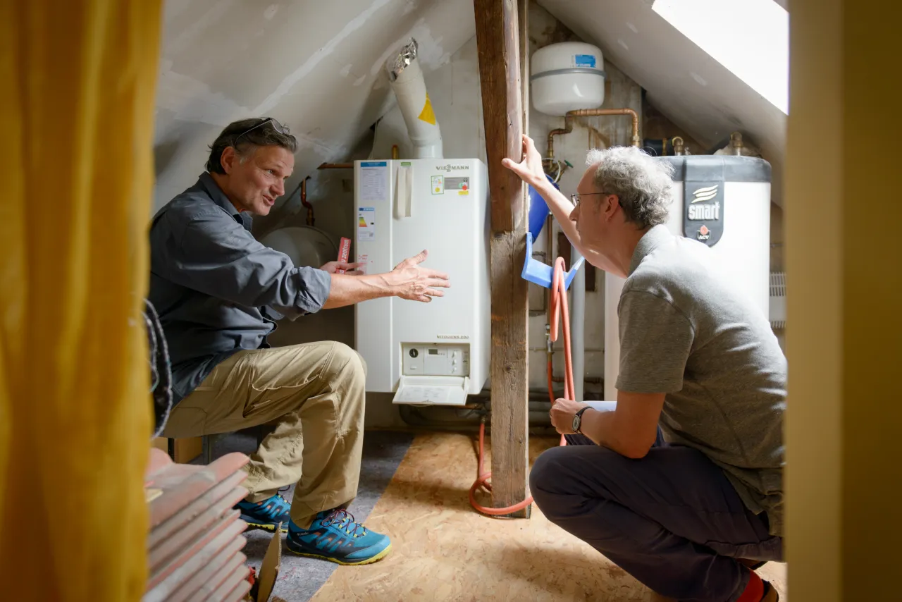 Beratungssituation: Zwei Männer knien vor Heizungsanlage.