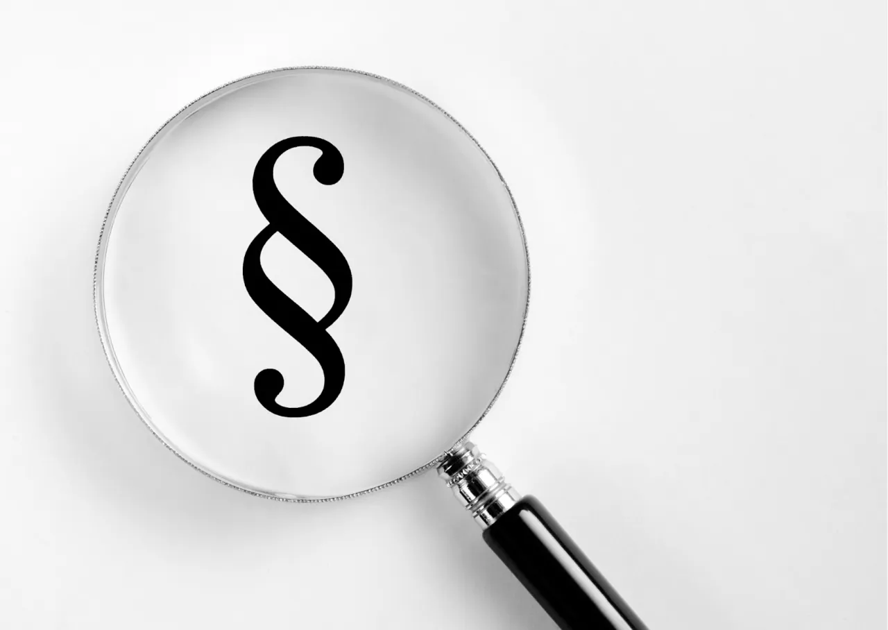 Ein Paragraphensymbol unter einer Lupe: Das Gesetz wird genau betrachtet.