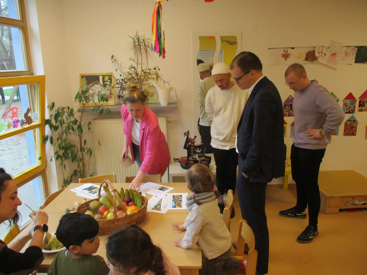 Staatsrat Jan Fries steht vor Gruppe Kindern, die am Tisch einen Obkorb und Blätter anschauen.