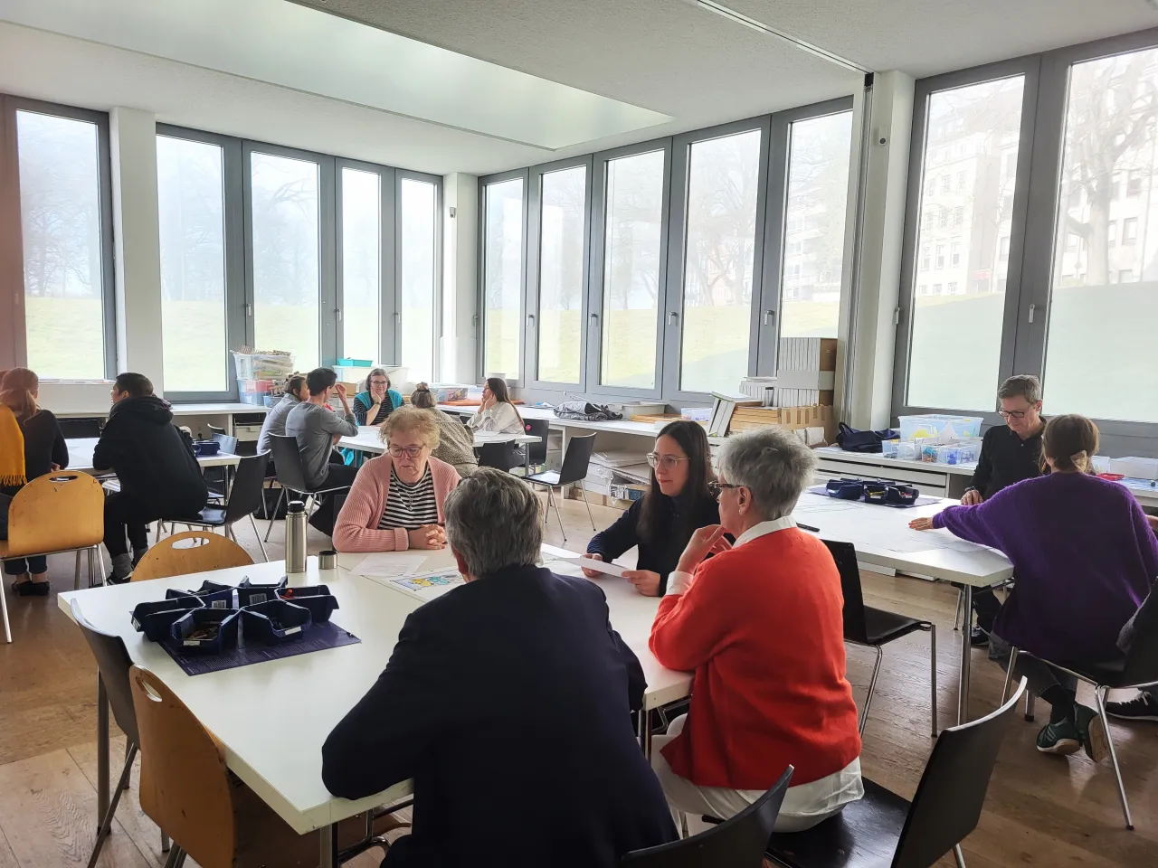 Menschen sitzen an Tischen und arbeiten in Kleingruppen