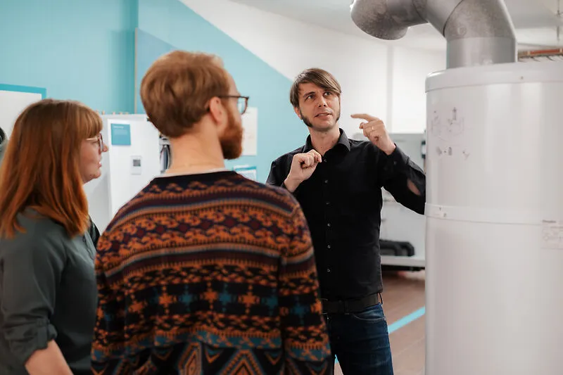 Mann erkl&auml;rt zwei weiteren Personen technische Details zu einem Heizsystem.
