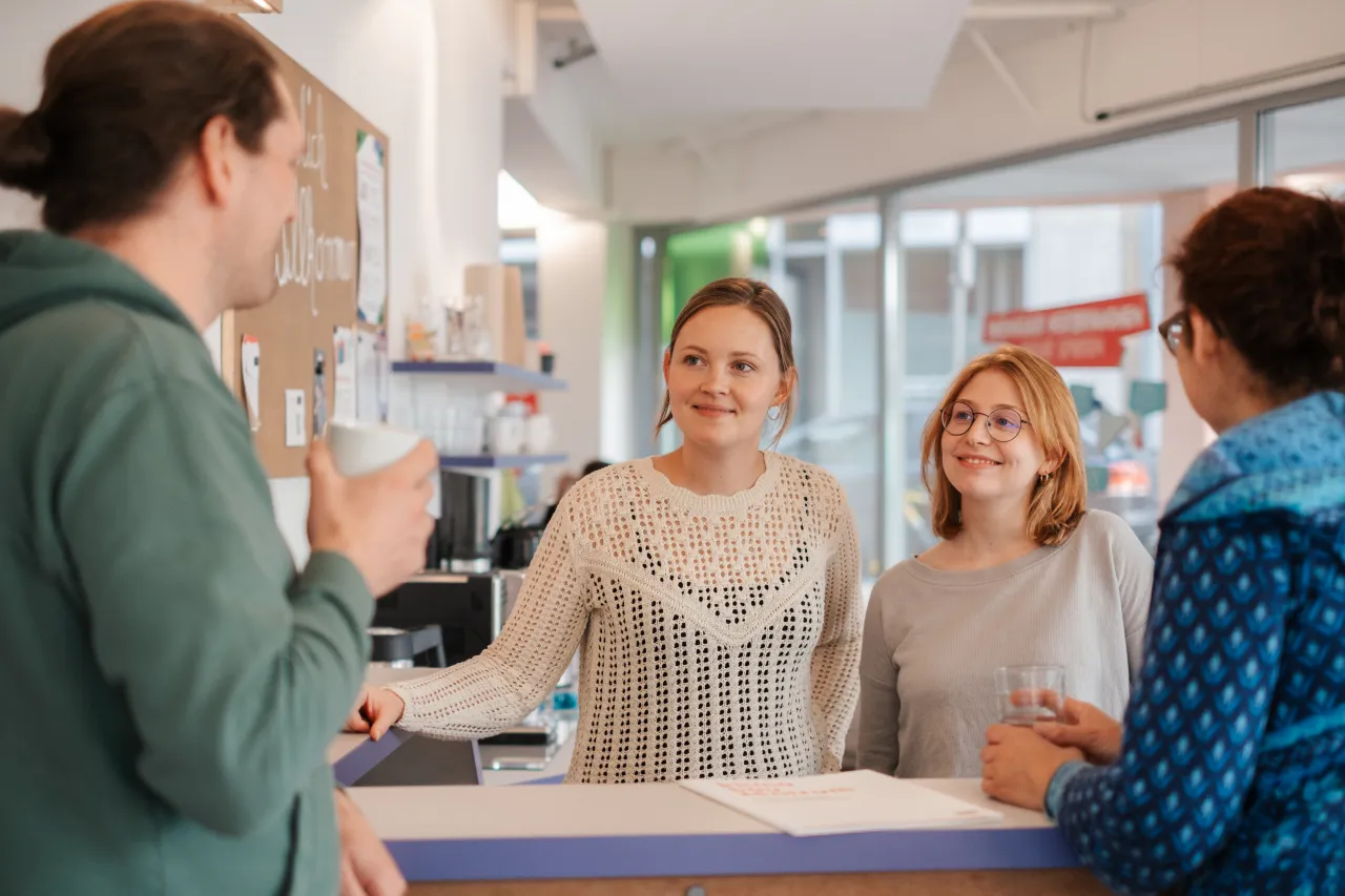 Vier Menschen stehen im Eingangsbereich am Tresen im Klima Bau Zentrum in Bremen und befinden sich im Gespr&auml;ch.