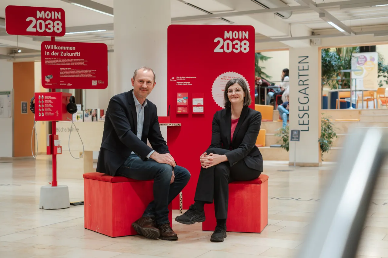 Martin Grocholl (Geschäftsführer von energiekonsens) und Lucia Werder (Direktorin der Stadtbibliothek Bremen) vor der neuen Hörstation „Moin 2038“ in der Zentralbibliothek.