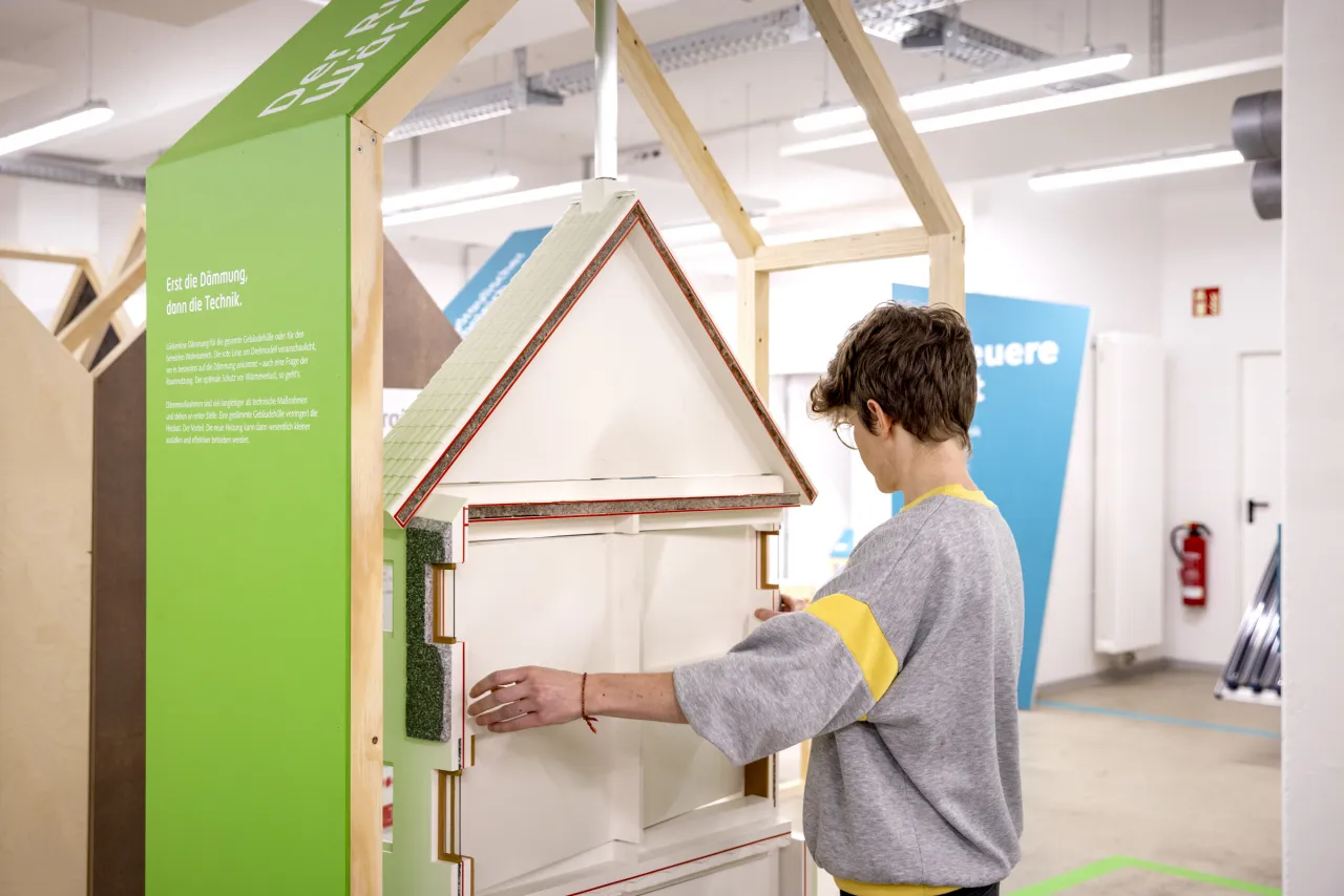 Person steht vor einem Hausmodell, das unterschiedliche Dämmebenen zeigt