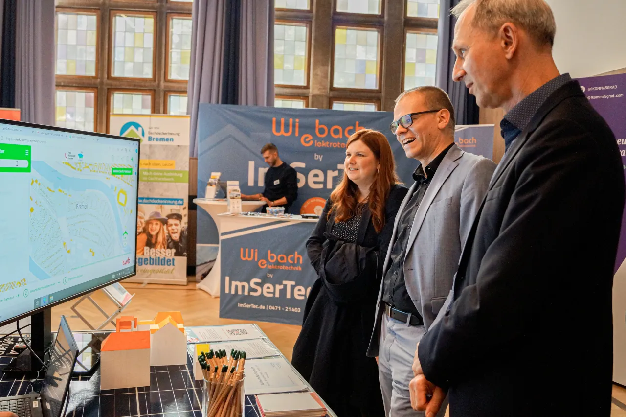 Jan Fries steht zwischen Anne Tillery und Martin Grocholl und blickt auf einen Bildschirm an der linken Seite.