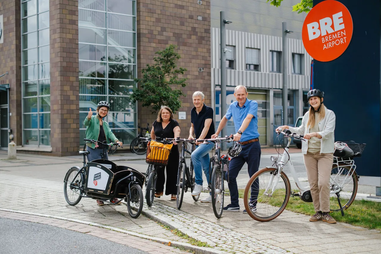 F&uuml;nf Menschen mit Fahrr&auml;dern stehen vorm Bremer Flughafen und starten von hier aus mit einer Radtour