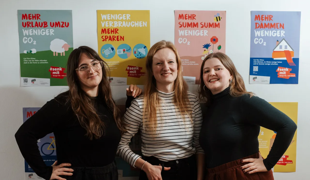 #senkmit Team Lena, Friderike und Luise steht vor Wand mit Kampagnenplakaten