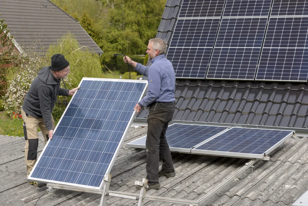 Zwei Personen auf einem Hausdach installieren ein Solarpanel