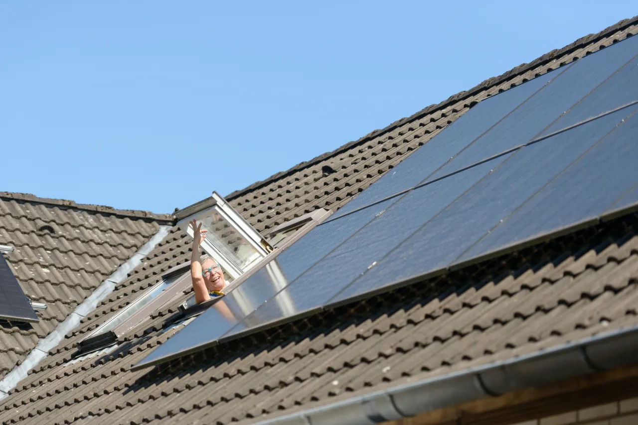 Eine Frau schaut aus einemDachfenster, daneben sind auf dem Dach Solarmodule zu sehen.