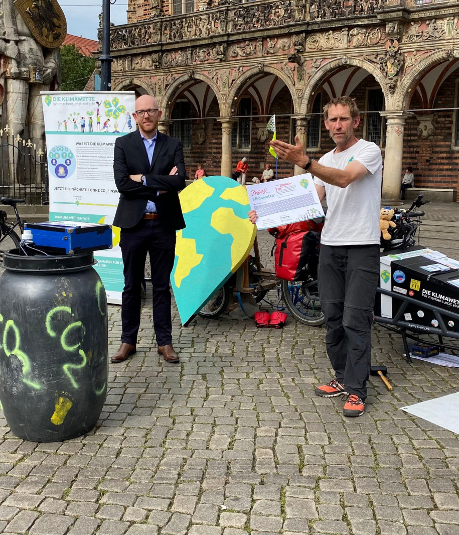 Pressefoto: Staatsrat Ronny Meyer steht vor Tonne, die mit CO2 beschriftet ist, daneben Initiator der Klimawette