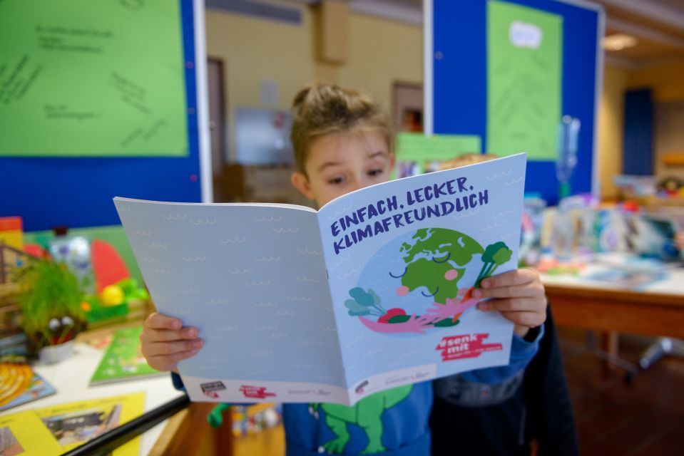 Kind hält das Klimakochbuch: Einfach, lecker, klimafreundlich, in den Händen.