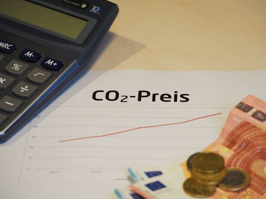Taschenrechner, Geldscheine und Münzen auf einem Graphen, der die Entwicklung des CO2-Preises anzeigt