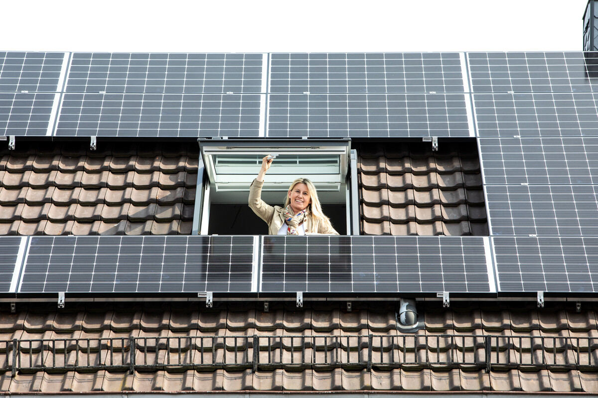 Frau schaut aus Dachfenster neben Solarmodulen
