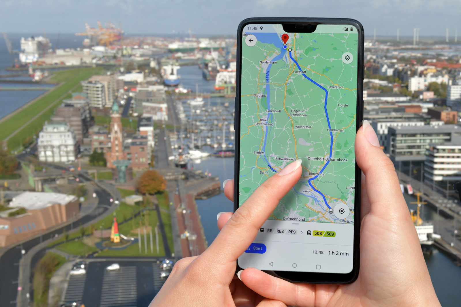 Hand hält Smartphone mit mobiler Landkarte, Hafenbecken von Bremerhaven im Hintergrund