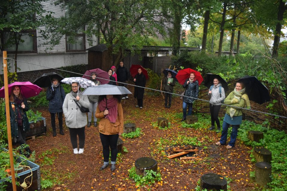 NRW-Delegation steht mit Regenschirmen im Gemeinschaftsgarten BlumenKOHL in Blumenthal