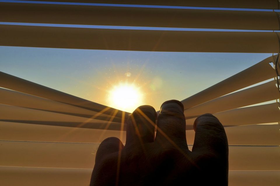 Finger zieht Jalousie runter, Sonne scheint durchs Fenster