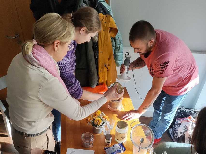 Zwei Frauen und ein Mann stehen an einem Tisch und packen Zutaten in einen Mixer
