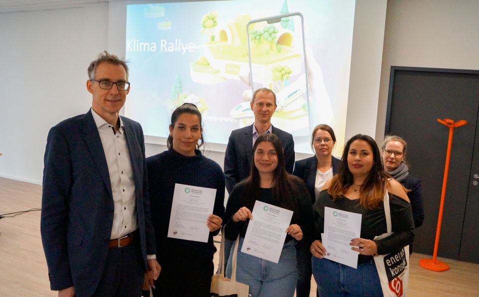 „Auszubildene stellen Klimaprojekte vor: Die Arbeitsgruppe „Klima Rallye“ (vorne) zusammen mit (v. l. n. r.) Staatsrat Martin Hagen, energiekonsens-Geschäftsführer Martin Grocholl, Katja Lessing, Direktorin der Verwaltungsschule und Hille Heumann-Klemm, Projektleiterin bei energiekonsens, bei der Abschlussveranstaltung im Projekt ‚Kommunale Klimascouts‘.“ (© energiekonsens)