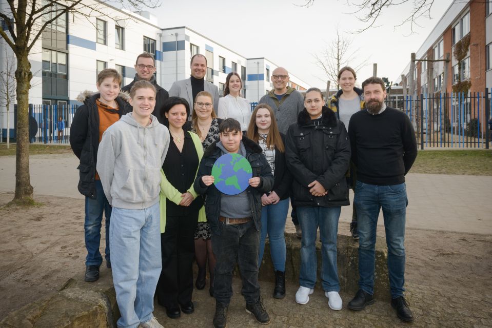 Gruppenfoto mit Schüler*innen, Lehrkräften, Schuldezernent Frost und Hannah Simon von der Klimaschutzagentur energiekonsens vor dem Gebäude der Heinrich-Heine-Schule in Bremerhaven